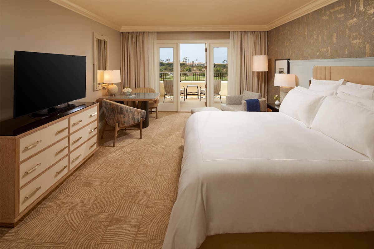 Habitación de hotel con una cama grande, televisión de pantalla plana, escritorio con silla y balcón con vistas al exterior.