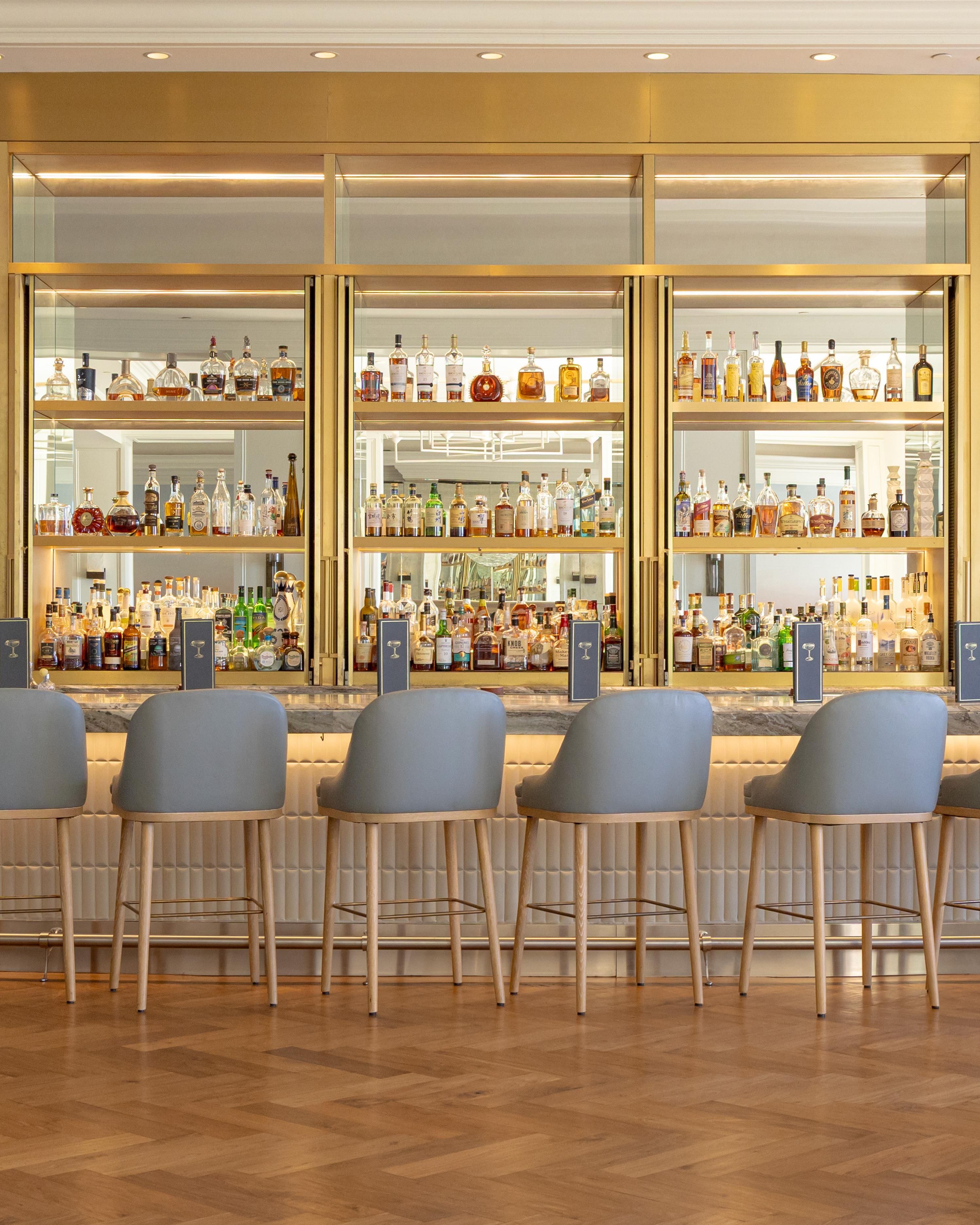 Un espace bar doté de plusieurs étagères remplies de bouteilles d’alcool, de tabourets de bar et d’un plancher en bois poli.