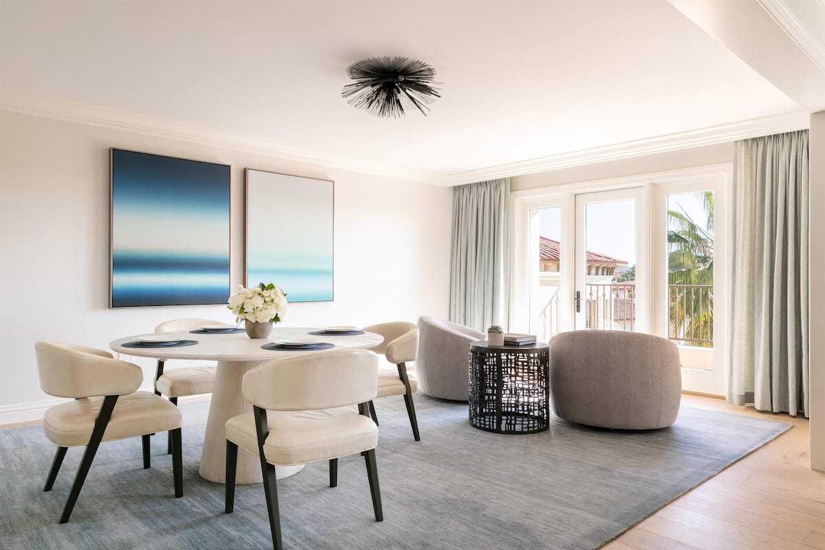 Una sala de estar moderna con una mesa de comedor redonda, sillas color beige, una mesa de centro redonda y un ventanal con cortinas.