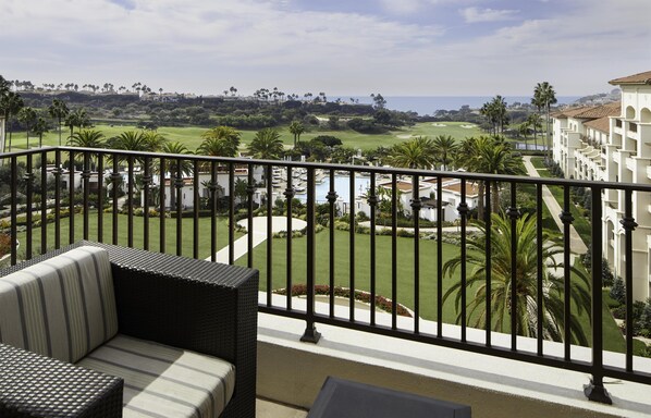 Ein Balkon mit Blick auf einen Golfplatz, ein Schwimmbad und ein Gebäude mit Ziegeldach.