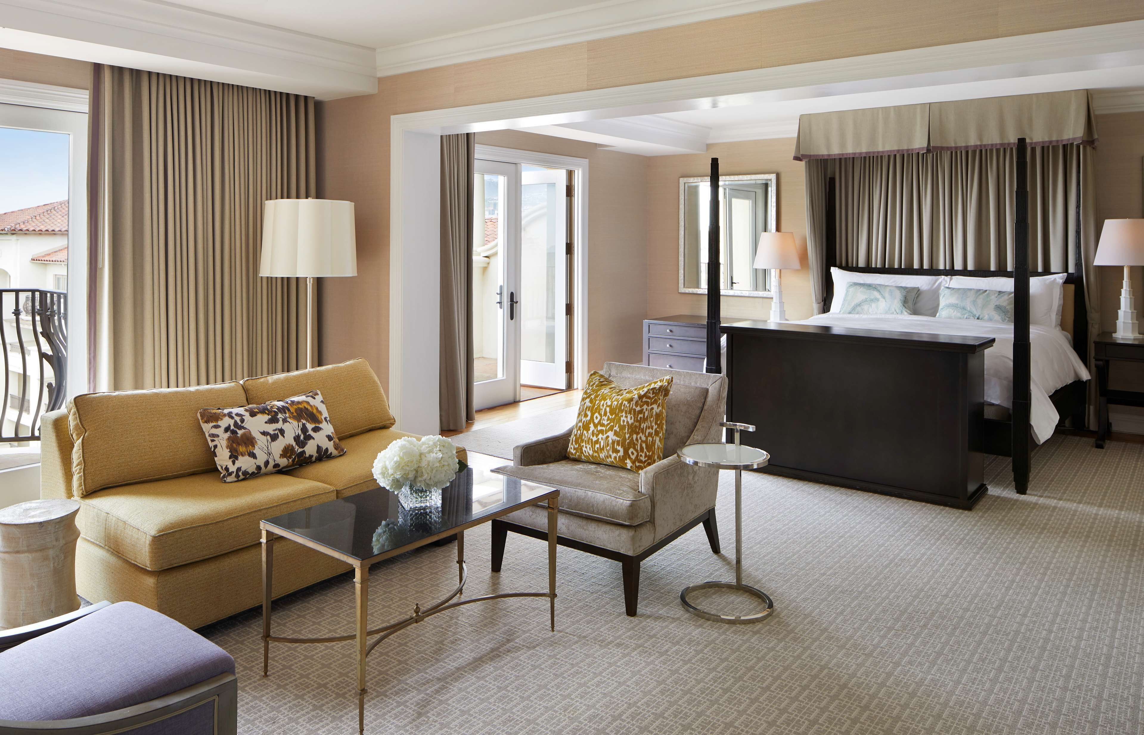 A hotel room with a sofa, armchair, coffee table, and a bed with a canopy.