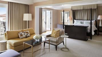 A hotel room with a sofa, armchair, coffee table, and a bed with a canopy.