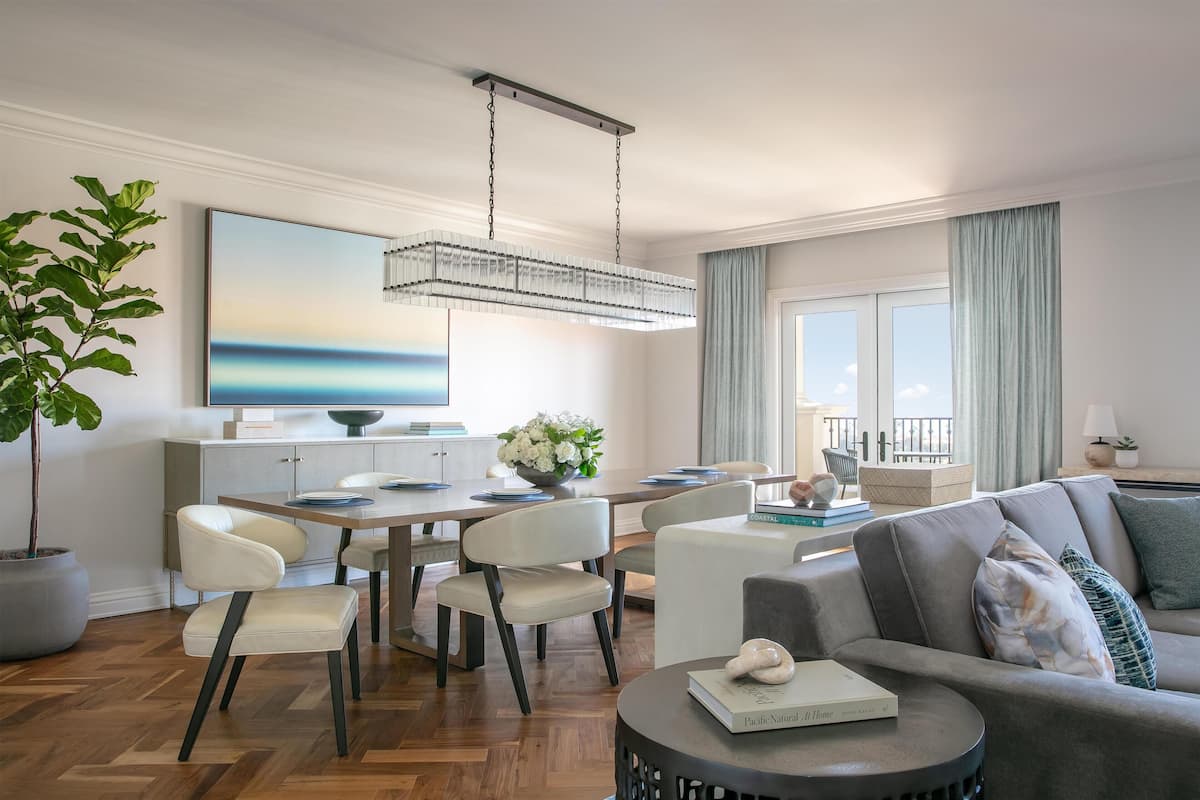 Una sala de estar moderna con comedor, que incluye una araña, un cuadro grande y vistas al exterior.
