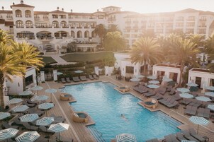 Zona de piscina en un resort con sillones reclinables y sombrillas, una piscina y un edificio con varios balcones.