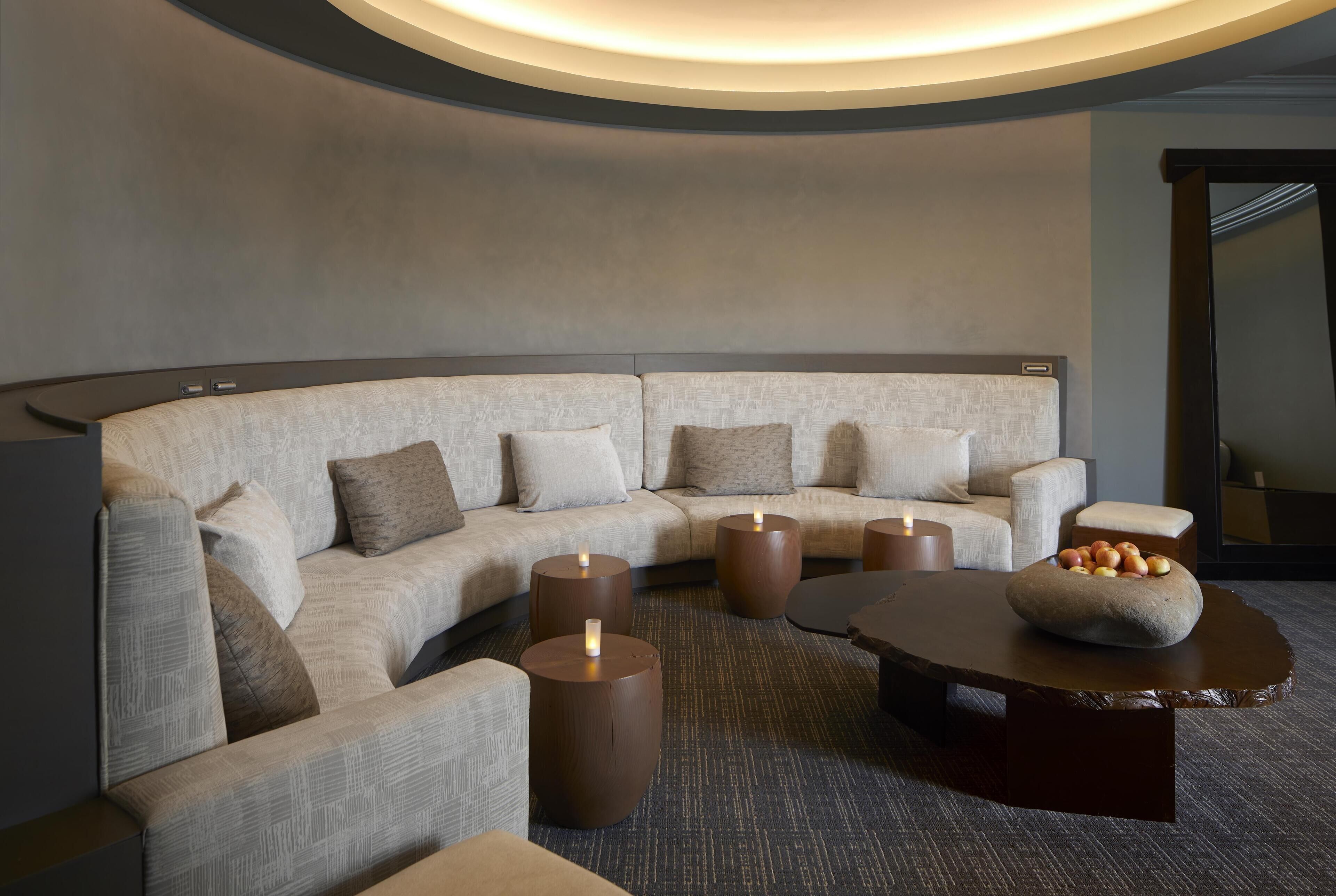 A modern, curved sectional sofa with a neutral color scheme, a round coffee table with a stone centerpiece, and a small side table with a candle.