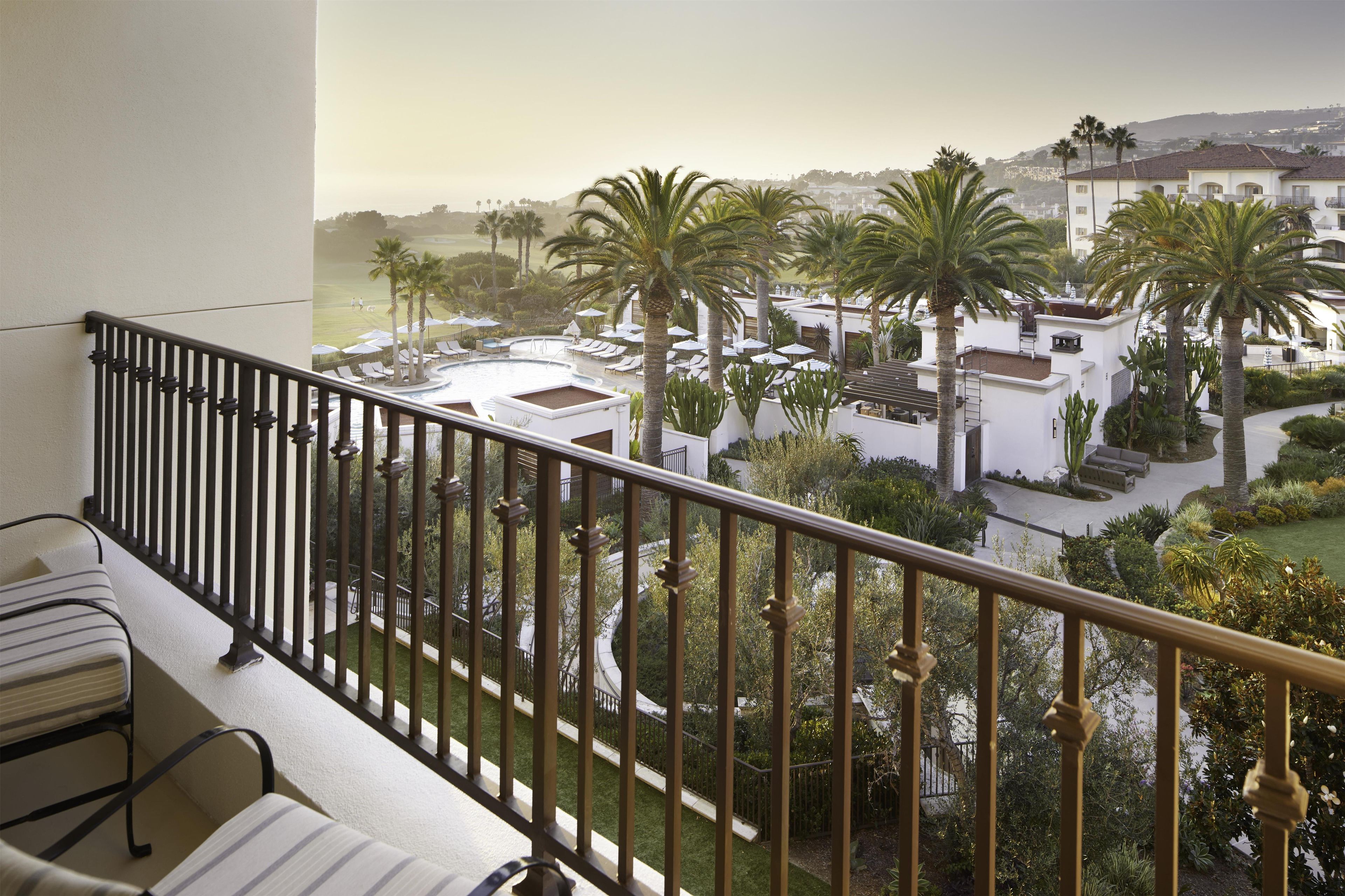 A balcony with a view of a pool area, palm trees, and surrounding buildings.