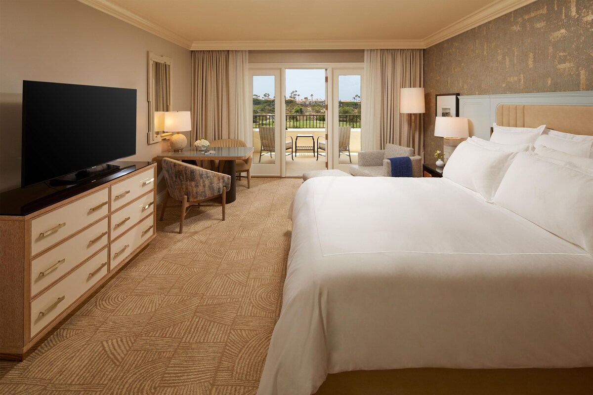 Ein Hotelzimmer mit einem großen Bett, einem Flachbildfernseher, einem Schreibtisch mit Stuhl und einem Balkon mit Blick ins Freie.