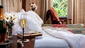 Un lit bien fait, recouvert d’une courtepointe à motifs floraux, un verre de champagne, une bouteille de champagne Cristal et un livre posé sur la table de chevet.