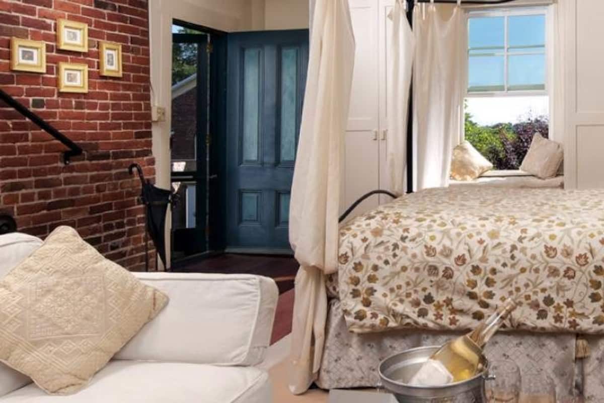 A bedroom with a bed, a nightstand, a lamp, a window with curtains, and a view of the outside.
