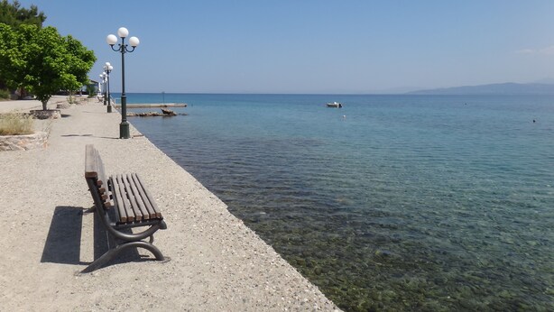 Una vista despejada de una playa de guijarros, con un banco de madera y farolas.