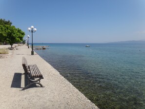 Una vista despejada de una playa de guijarros, con un banco de madera y farolas.