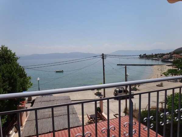 Vista costera desde un balcón con barandilla, una playa y un barco en el agua.