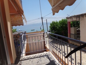 A balcony with a view of the sea, a tiled floor, and a metal railing.