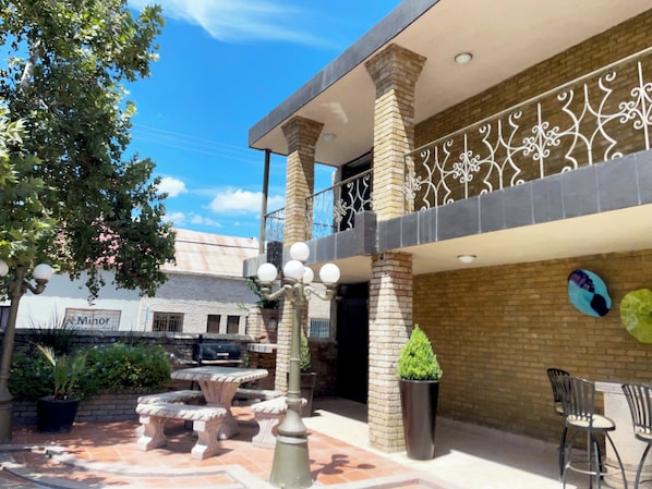A courtyard with outdoor seating, a brick wall, and a balcony with decorative railing.