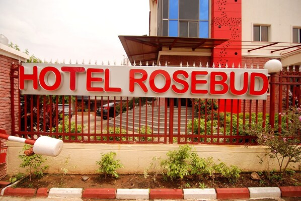 A hotel sign with the name "HOTEL ROSEBUD" in bold red letters on a white background, surrounded by a red metal fence with decorative elements.