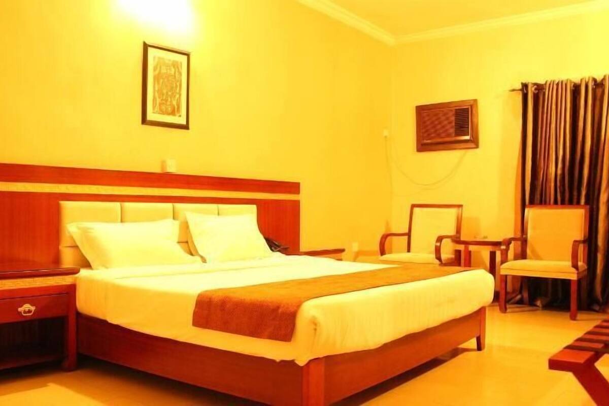 A hotel room with a wooden bed, a nightstand, a chair, a desk, and a TV.