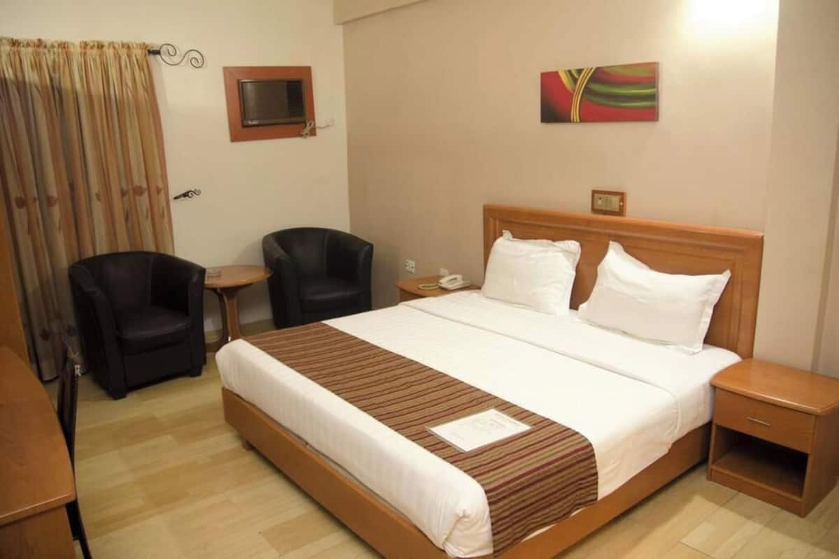 A hotel room with a single bed, a bedside table, a chair, a desk, a TV, and a painting on the wall.