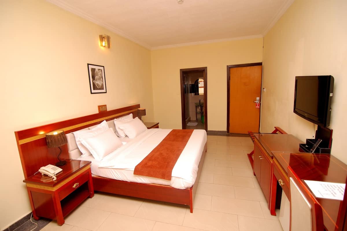 A hotel room with a bed, bedside table, lamp, TV, and a door leading to another room.