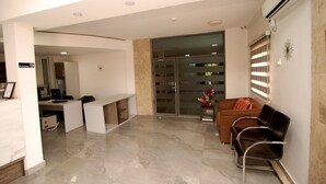 A reception area with a desk, chairs, a glass door entrance, and a wall-mounted air conditioning unit. - Hotel Rosebud (Abuja)