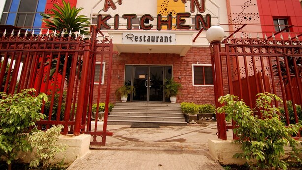 The entrance to the AFRICAN KITCHEN restaurant with a red metal gate, potted plants, and a clear view of the building's facade. - Hotel Rosebud (Abuja)