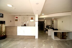 A modern reception area with a marble reception desk, a digital display, and a clean, minimalist design. - Hotel Rosebud (Abuja)