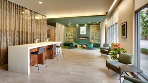 A modern kitchen with a central island, bar stools, and a seating area with green chairs and a sofa. - Hyatt House Portland/Downtown (Portland)