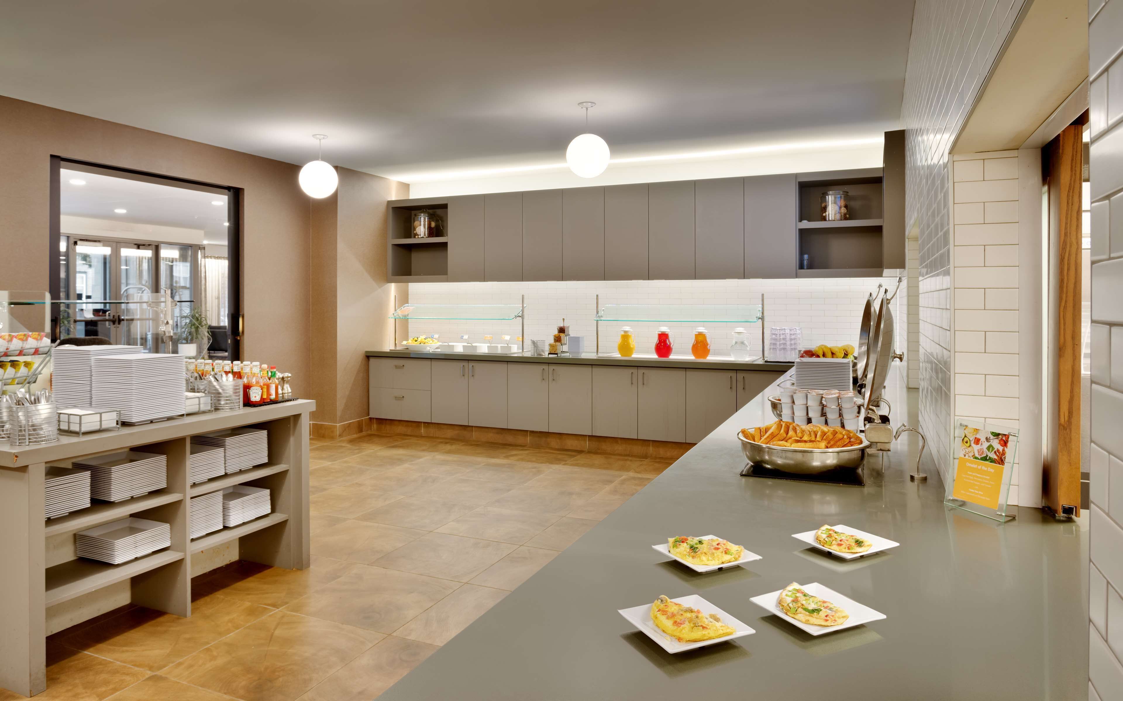 A modern breakfast area with a buffet setup, including plates of food, beverages, and condiments.