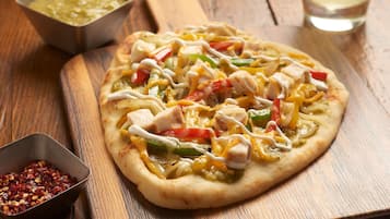 A pizza with various toppings on a wooden board, accompanied by a drink and a salad on a wooden table.