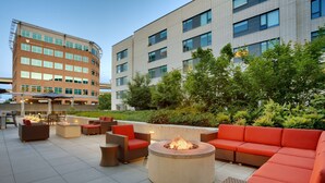 An outdoor patio area with seating, a fire pit, and a view of a multi-story building in the background. - Hyatt House Portland/Downtown (Portland)