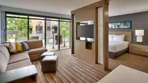 A modern hotel room with a sofa, ottoman, TV, bed, and a large window offering a view of the outside. - Hyatt House Portland/Downtown (Portland)