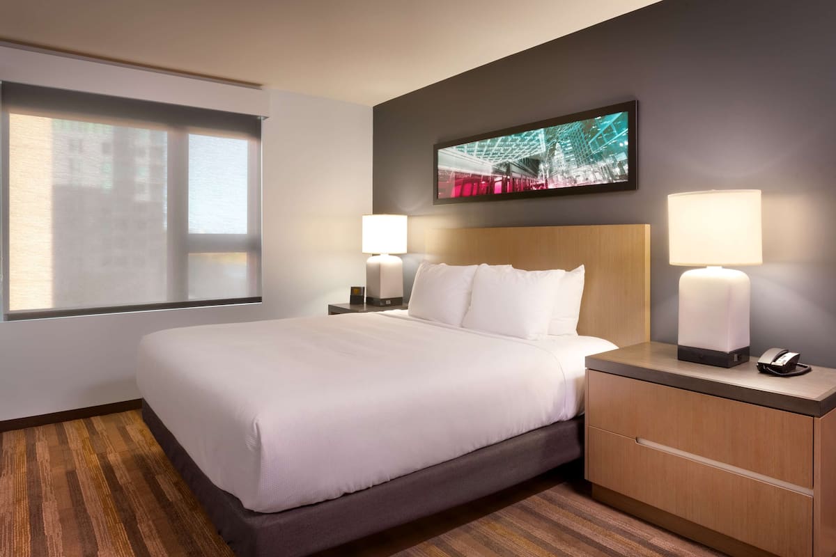 A hotel room with a large bed, two bedside lamps, a nightstand with a phone, and a TV mounted on the wall.