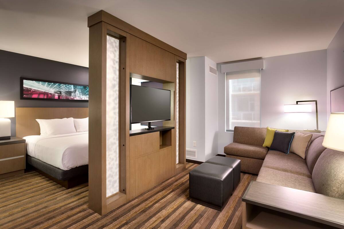 A hotel room with a bed, a sofa, a television, and a window.