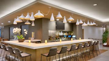 Uma área de bar moderna com um balcão comprido, vários bancos e iluminação pendente.
