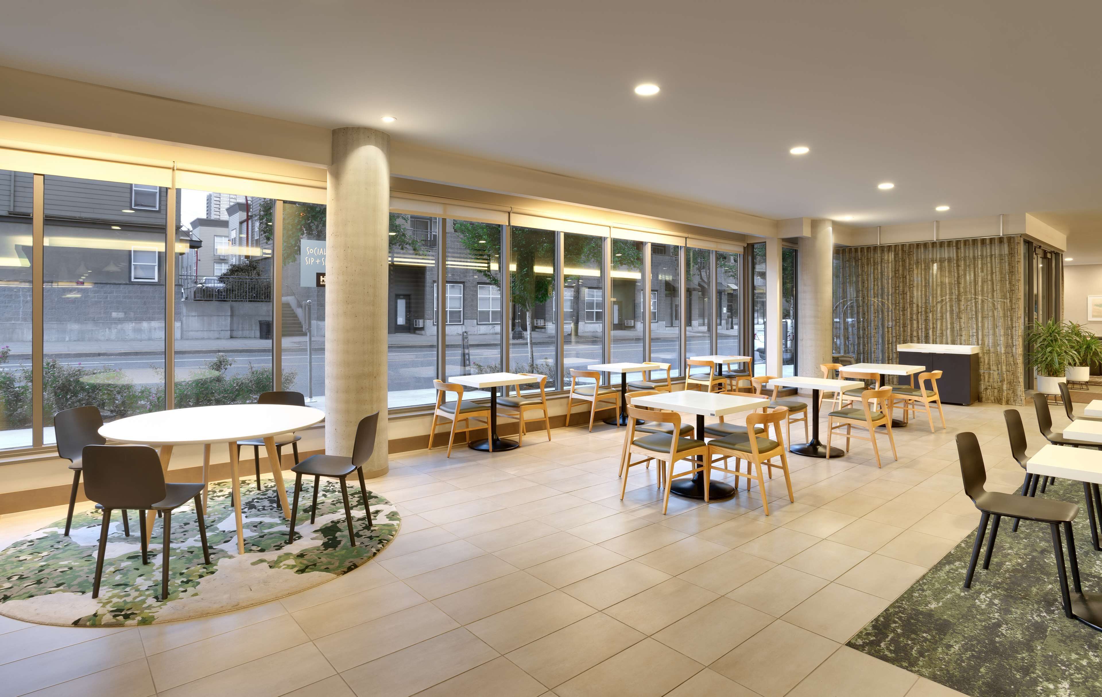 Un moderno vestíbulo de hotel con amplios ventanales, varias zonas de estar y una columna central.