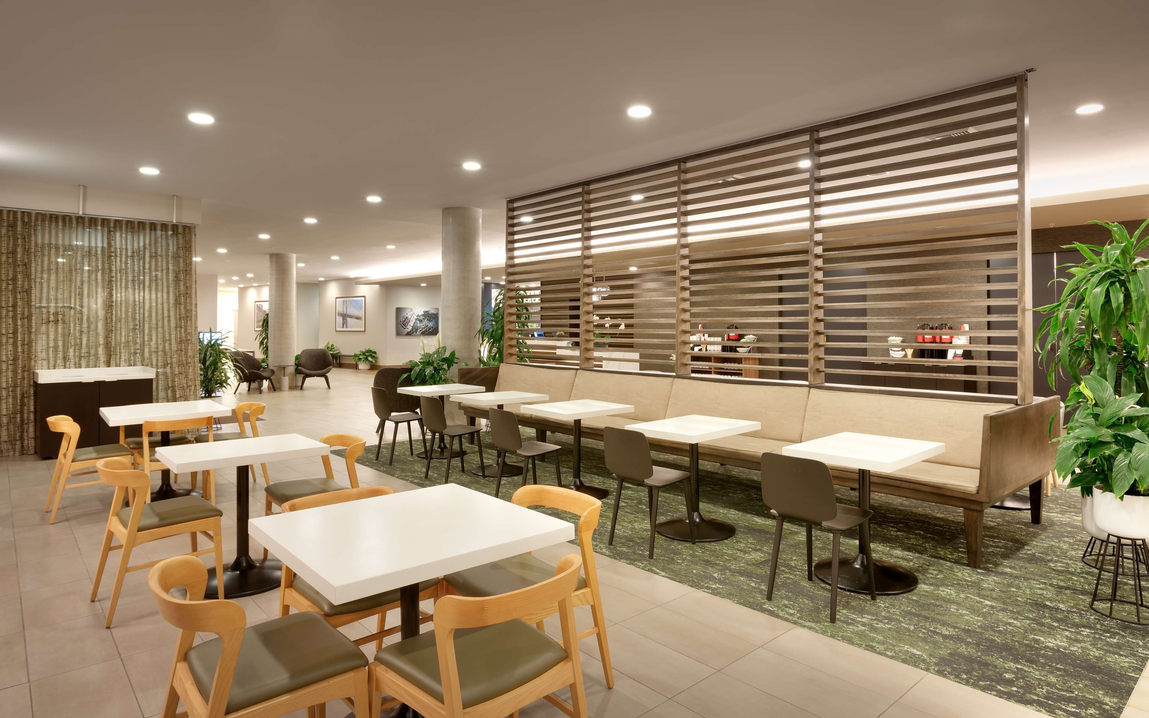 A modern restaurant with multiple tables and chairs, a decorative wall with slats, and potted plants.
