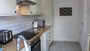 Una cocina compacta con armarios blancos, microondas, tostadora y escurreplatos.