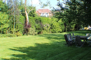 A well-maintained lawn with a dining table and chairs, surrounded by dense shrubbery and trees. - Moleside Cottage (Tonbridge)