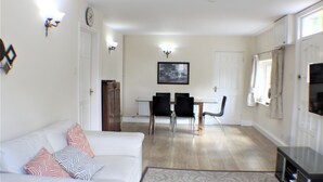 Una sala de estar con un sofá blanco, cojines estampados, una mesa de comedor con sillas y un televisor.