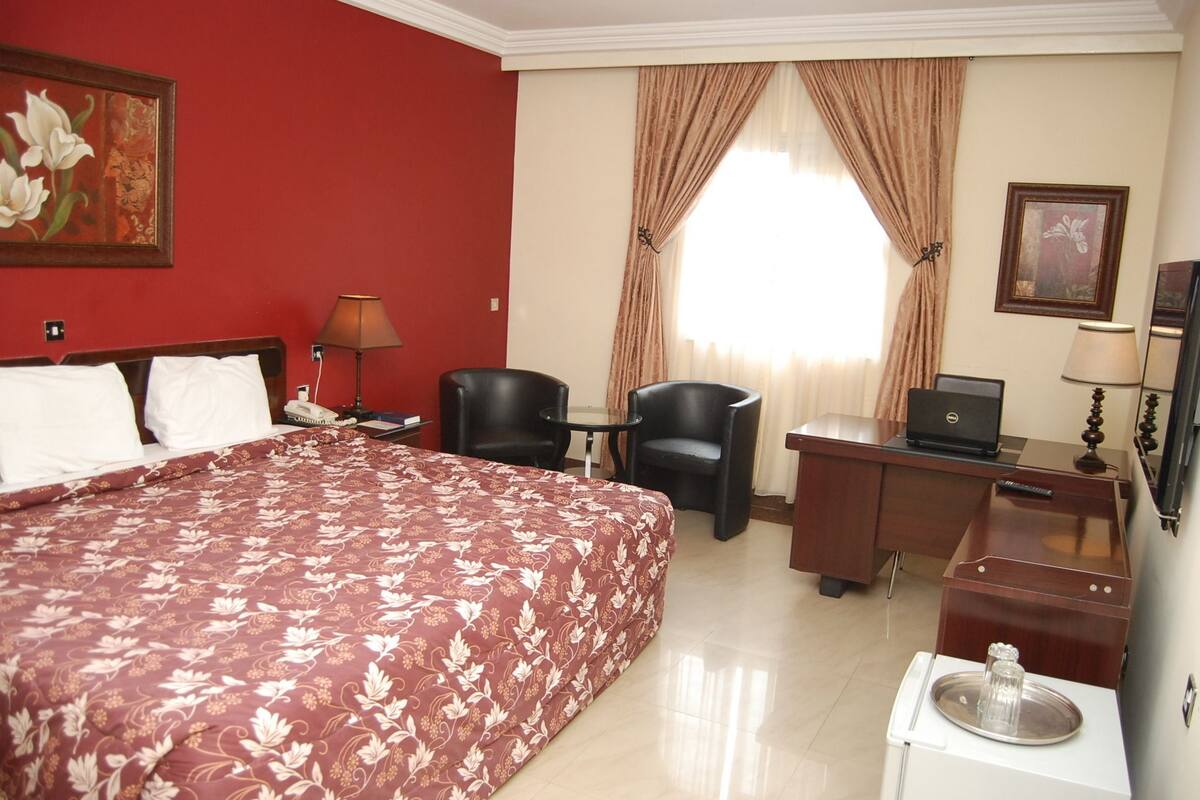 Une chambre d’hôtel avec un grand lit, un bureau avec un ordinateur portable, une chaise, une petite table avec un verre et un téléphone.