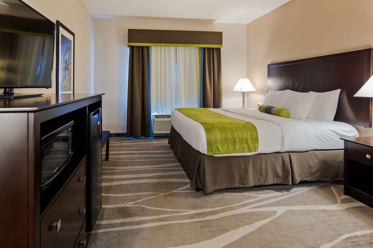 Habitación de hotel con cama, televisor, escritorio y ventana con cortinas.