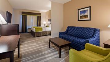 A hotel room with a bed, a sofa, a desk, and a chair. There is a window with curtains, a picture on the wall, and a television on a stand.