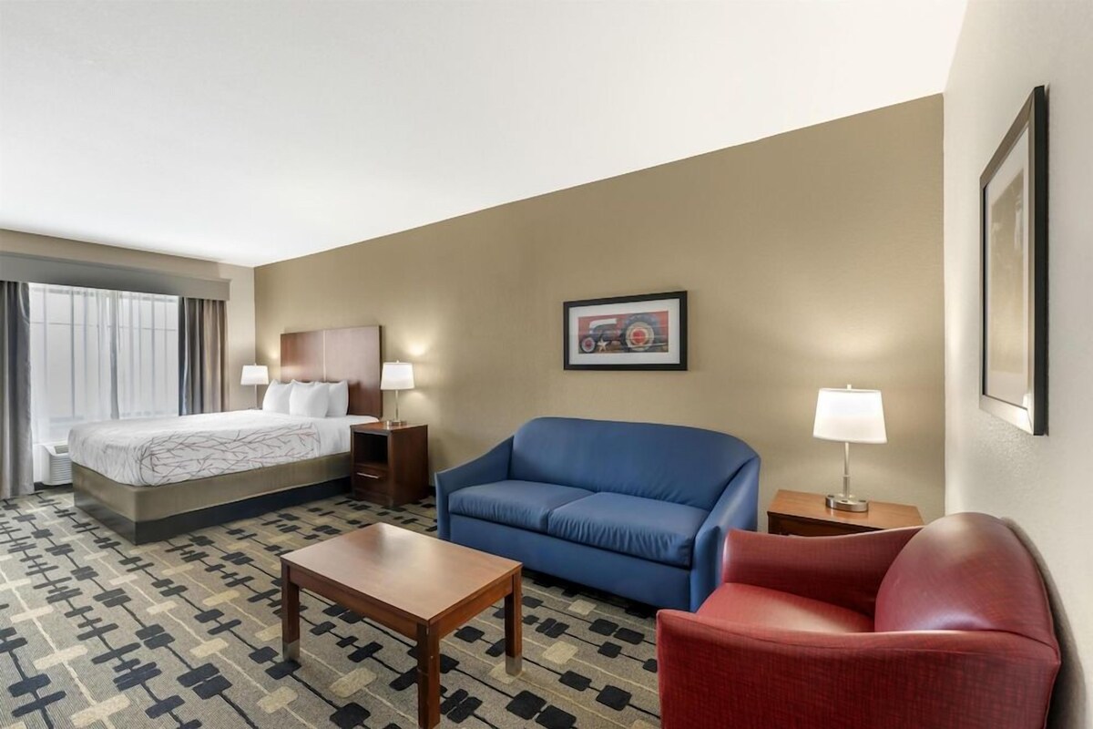 A hotel room with a bed, a blue sofa, a red armchair, a wooden table, and a patterned carpet.