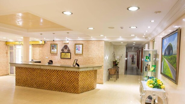 Zona de recepción con mostrador de check-in, certificados enmarcados en la pared y una mesa decorativa con flores.