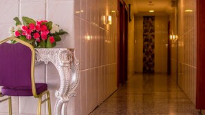 Un pasillo de hotel con una silla morada, una mesa blanca ornamentada y un ramo de flores.