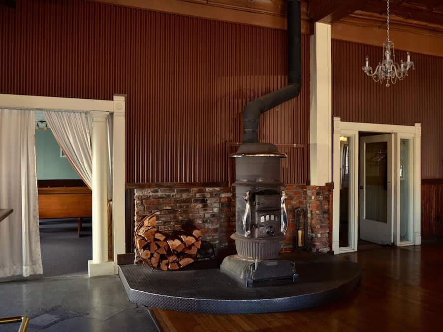 A room with a wood-burning stove, a brick fireplace, a chandelier, and a door leading to another room.