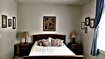 A bedroom with a bed, two nightstands, a ceiling fan, and framed pictures on the walls.