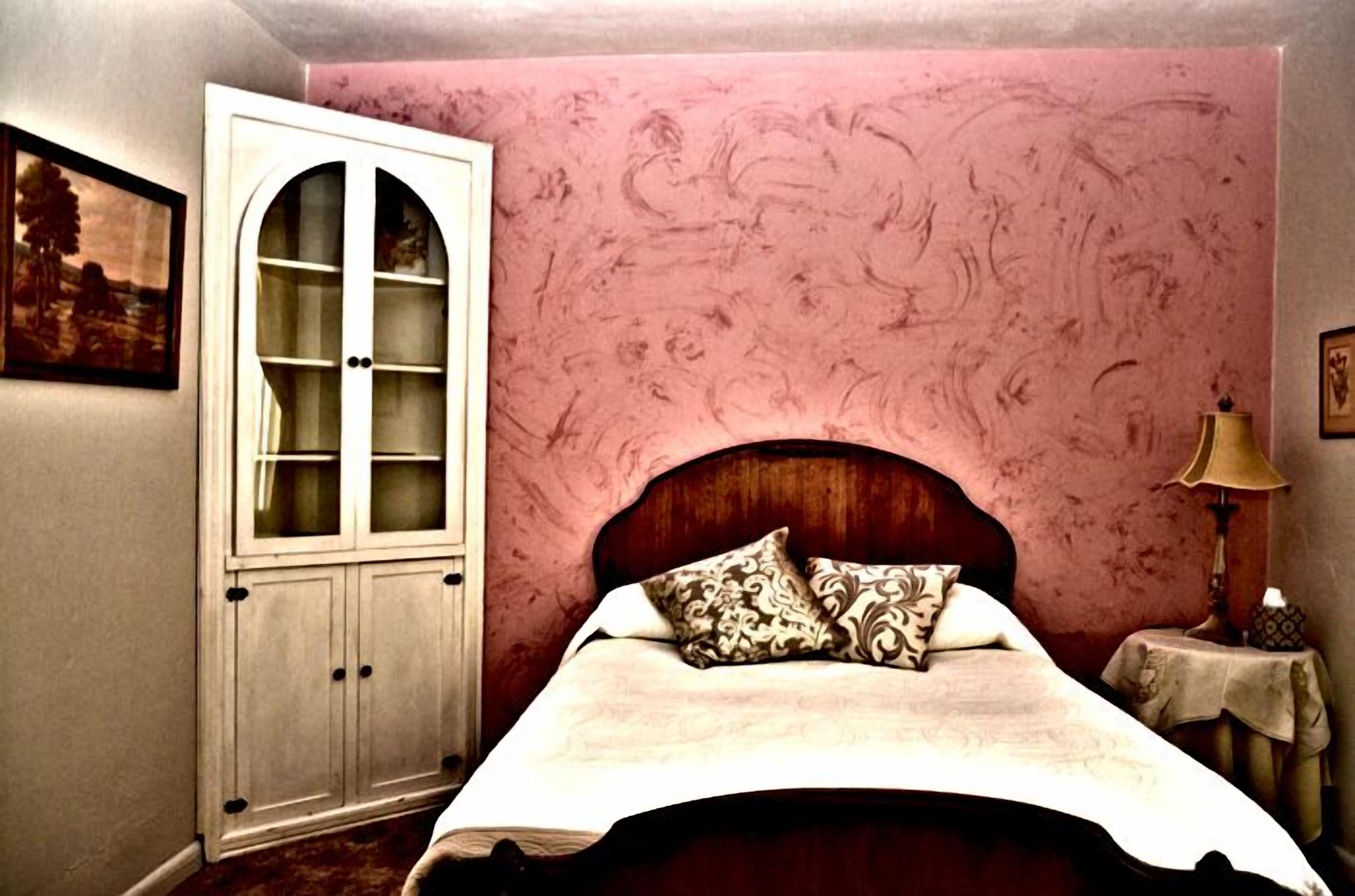 A bedroom with a wooden bed, a white cabinet with glass doors, and a pink textured wall.
