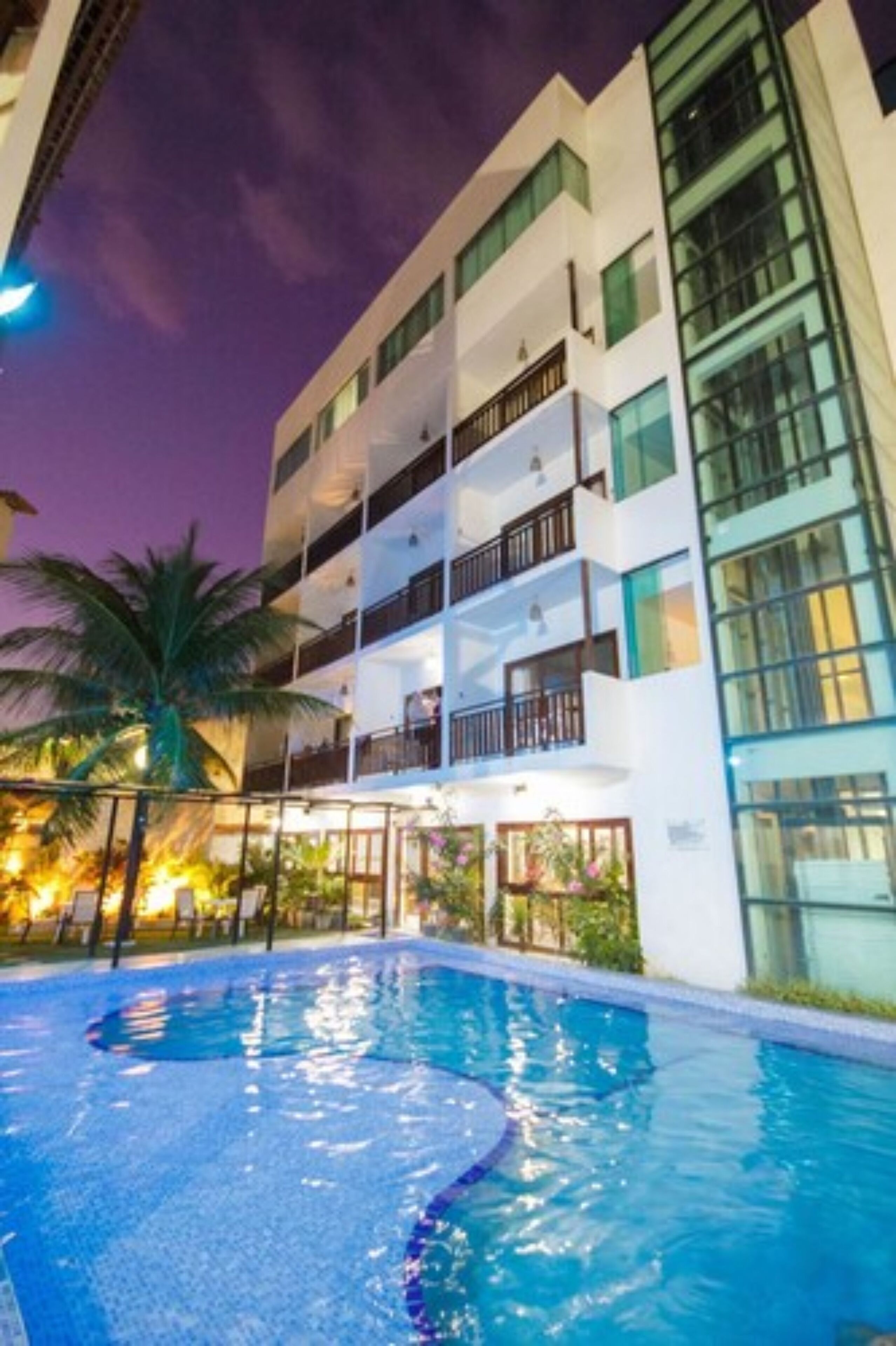 A modern hotel with a swimming pool, multiple balconies, and lush landscaping.