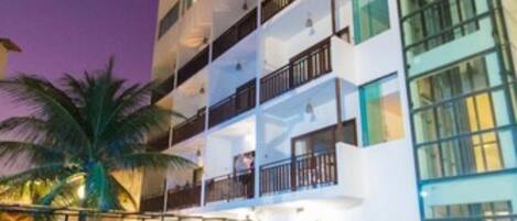 A modern hotel with a swimming pool, multiple balconies, and lush landscaping.