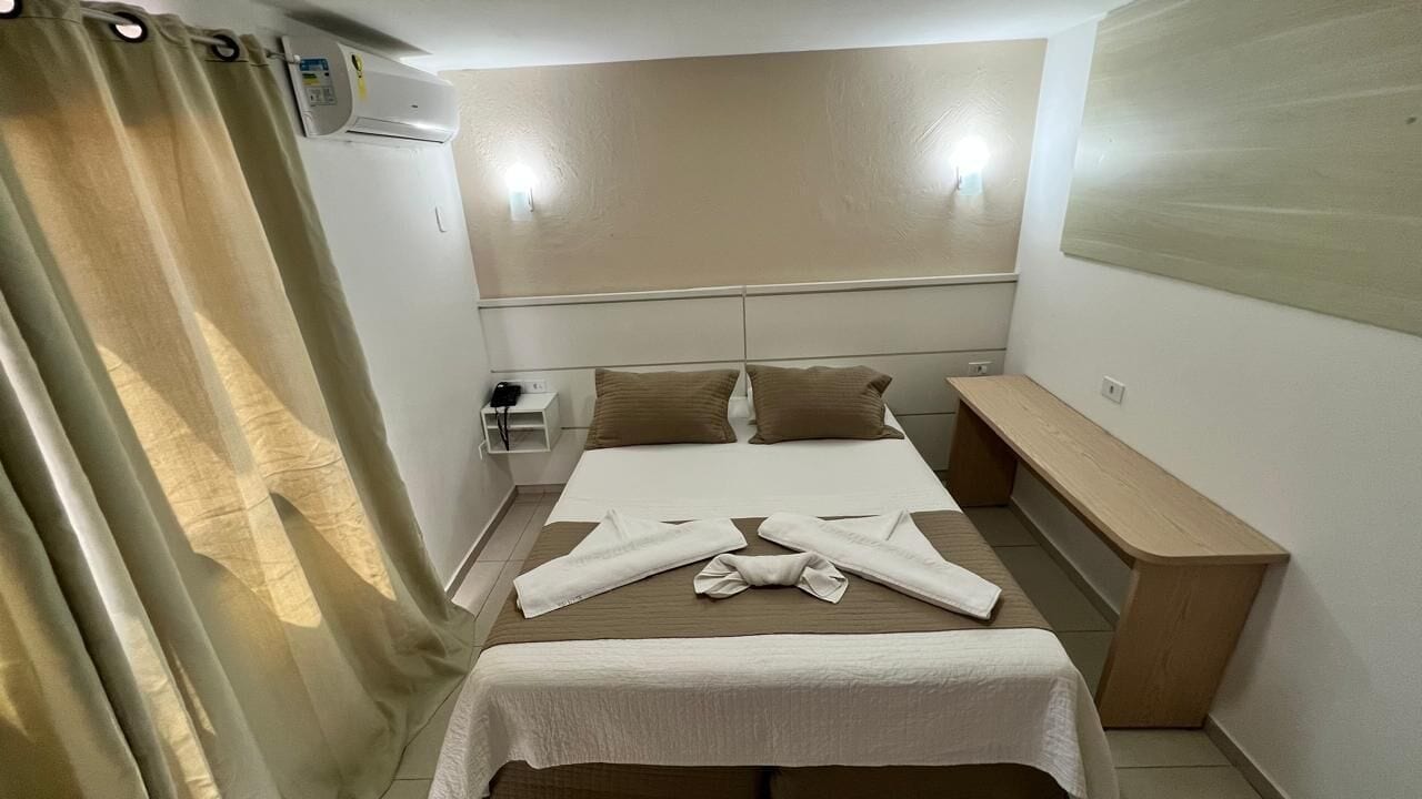 A hotel room with a bed, a bedside table, a bench, and a curtain.